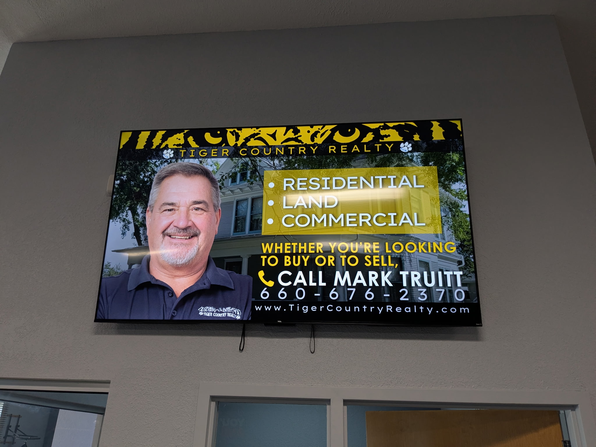 AdSync digital screen mounted on wall showing Tiger Country Realty advertisement